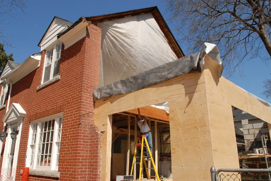 Work in progress on a home addition, featuring new wood framing with a construction worker on a ladder.